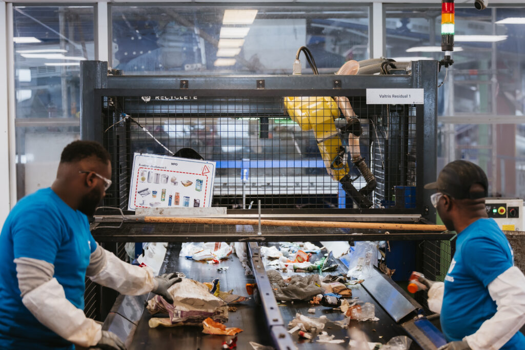 A waste picking robot on a conveyor belt next to human workers